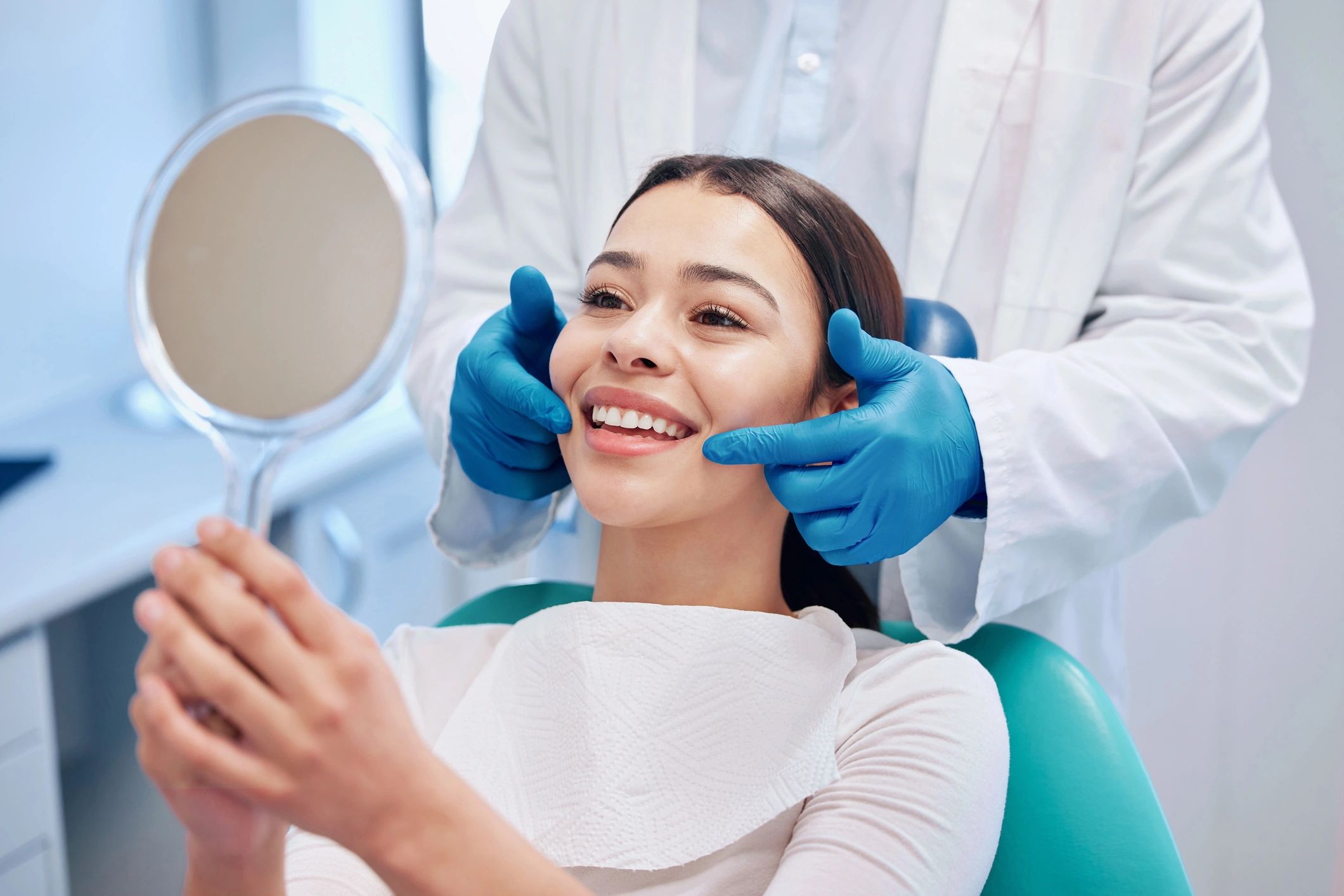Smiling woman in a dental chair viewing her new smile in a hand mirror